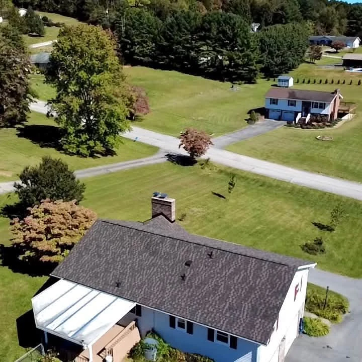 Alternate aerial project photograph of the same white home's shingle roof, showing the ridge, chimney and covered rear patio.