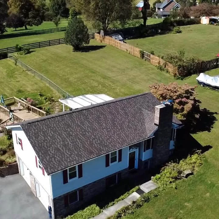 Drone project photograph of a white home with a dark shingle gable roof, red shutters and a brick chimney.